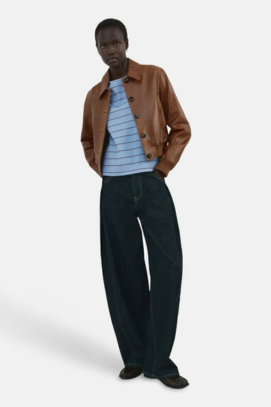 T-shirt bleu rayé de MANGO, associé à une veste en cuir marron et un jean bleu foncé ample.