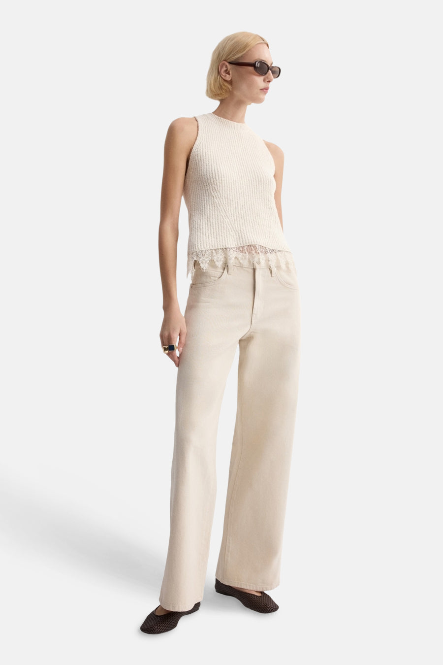 Haut écru sans manches de MANGO, fini avec des détails en dentelle, porté avec un jean beige ample et des chaussures marron.