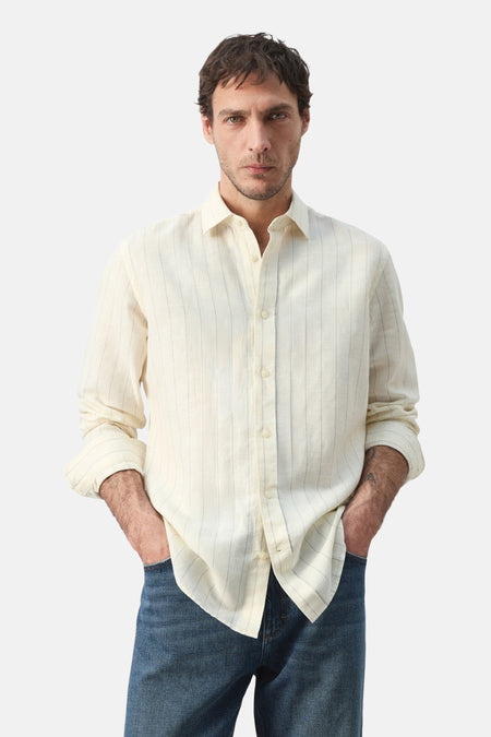 Chemise écru à manches longues de MANGO, rayée, avec manches retroussées et portée avec un jean.