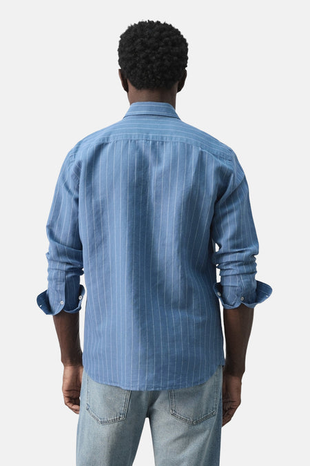 Blauw gestreept overhemd van MANGO, gezien vanaf de achterkant met opgerolde mouwen en een jeans.
