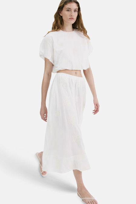 Jupe longue écru de MANGO avec de subtiles broderies blanches, combinée à un crop top assorti.