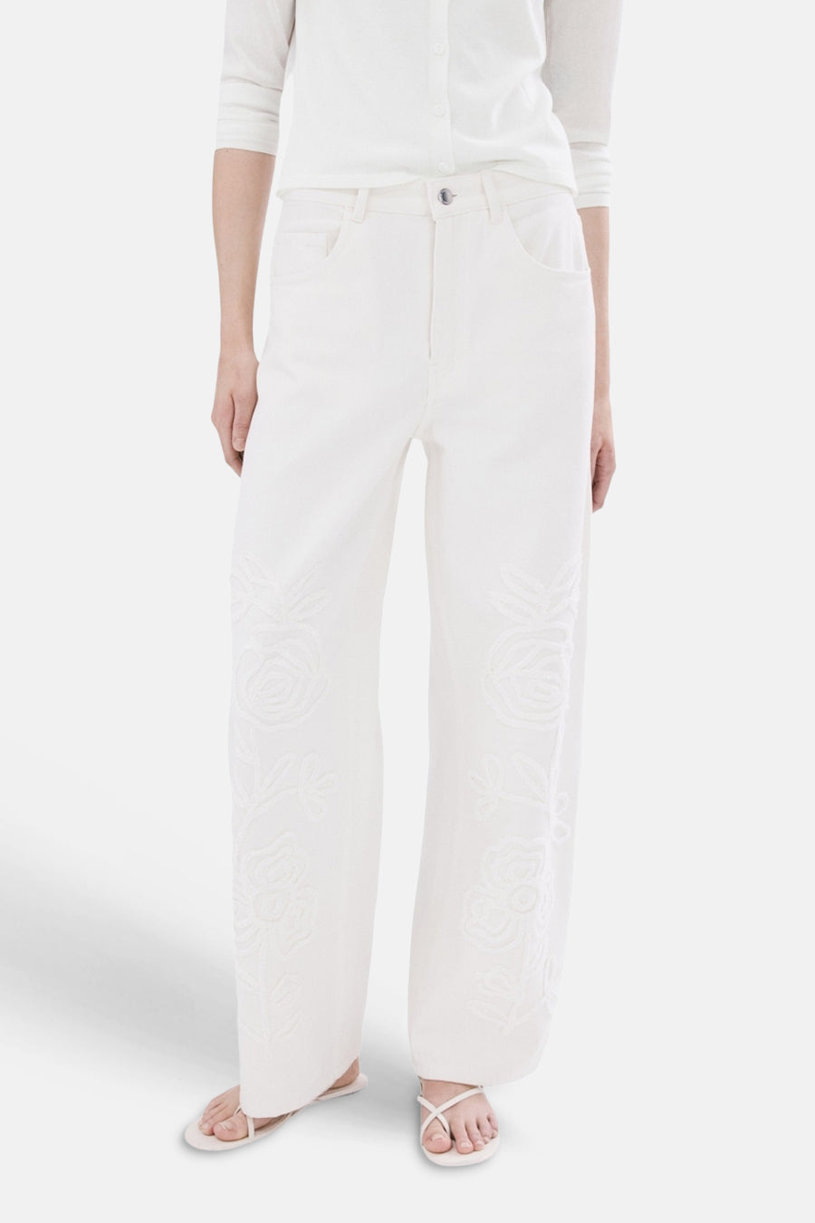 Jean large en denim blanc cassé de MANGO, vu de dos, porté avec un haut blanc et des sandales.