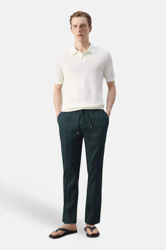 Pantalon vert foncé de MANGO avec cordon de serrage et plis verticaux, stylisé avec un polo blanc et des tongs noires.