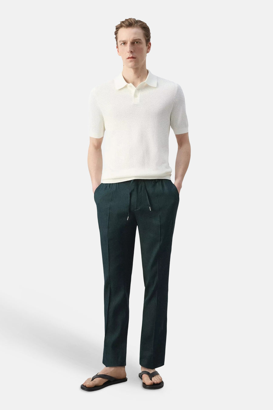 Pantalon vert foncé de MANGO avec cordon de serrage et plis verticaux, stylisé avec un polo blanc et des tongs noires.
