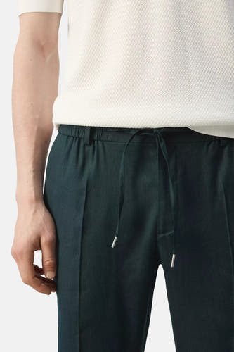 Pantalon vert MANGO avec taille à cordon de serrage, embouts argentés et porté avec un t-shirt blanc texturé.
