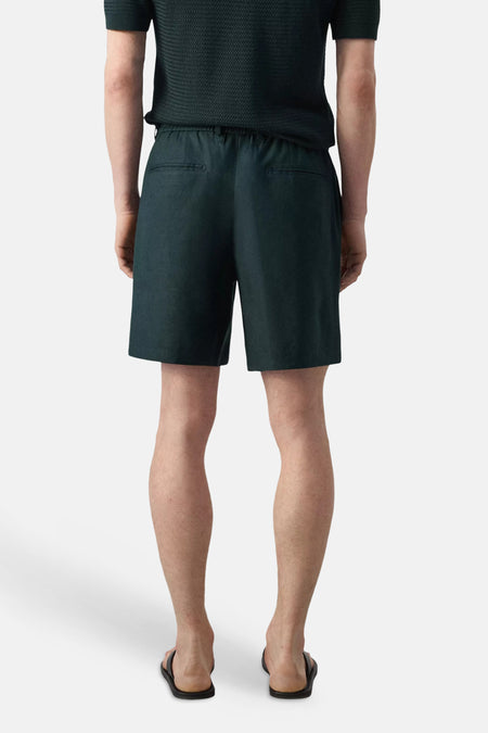 Groene Bermuda's van MANGO, achterkant met twee zakken, model draagt donkergroen shirt en slippers