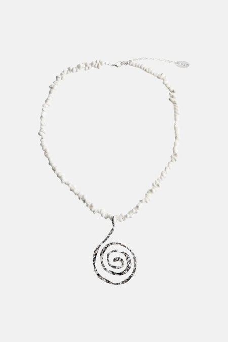 Collier court de perles blanches de MANGO, avec pendentif spirale argentée, porté sur un haut de bikini rose clair.