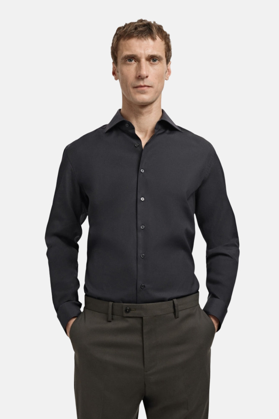 Man in zwarte overhemd en groene broek, handen in zakken, productafbeelding.
