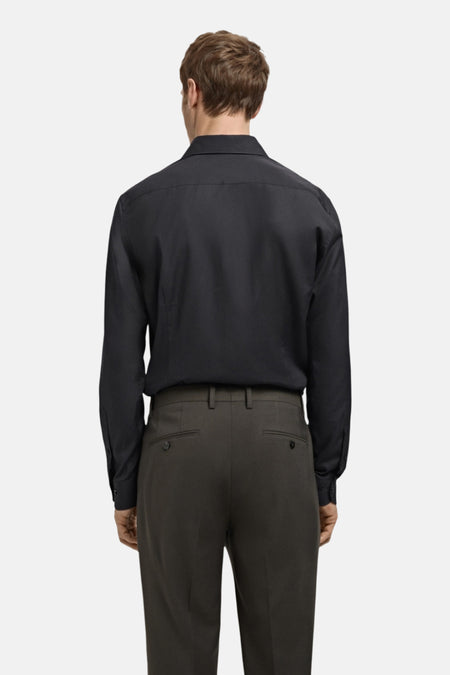 Achterkant van een man in een zwart overhemd en grijze pantalon.