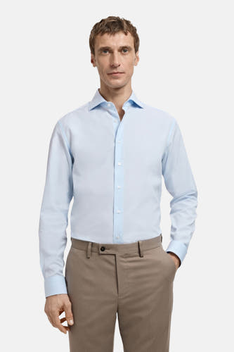 Chemise bleue à manches longues de MANGO, portée sous un manteau brun.