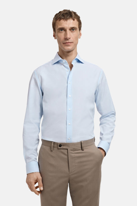 Man draagt lichtblauw overhemd en bruine pantalon.