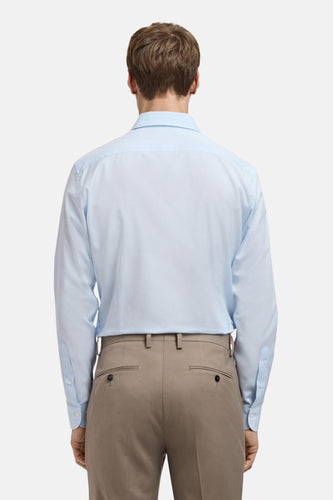 Achterkant van een man in een lichtblauw overhemd en beige broek.