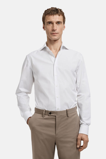 Man in wit overhemd en beige pantalon, staand.
