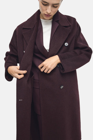 Manteau rouge long de MANGO, avec une double rangée de boutons, porté sur un haut blanc et un pantalon rouge.