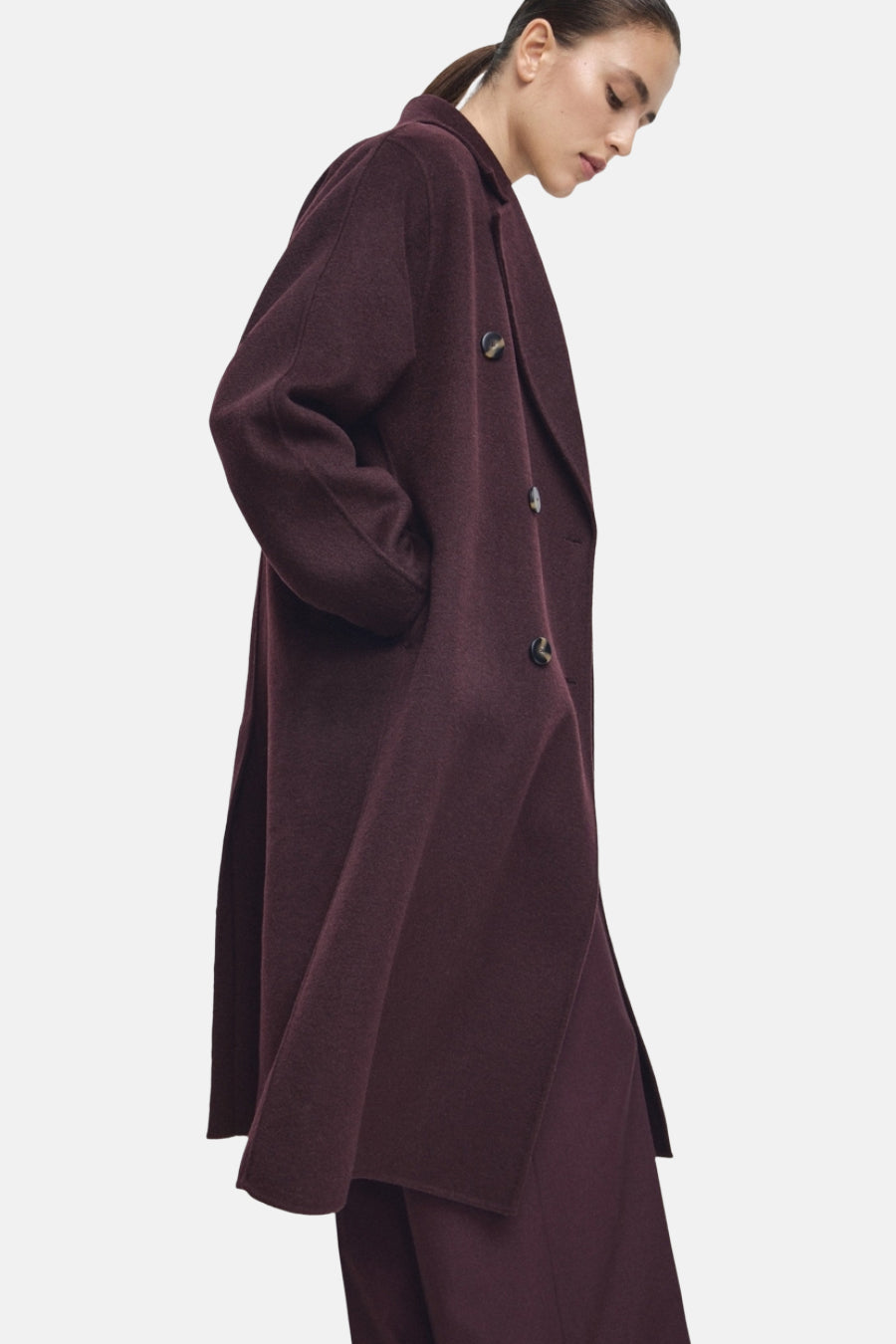 Long manteau rouge de MANGO, avec des manches longues, une fermeture à boutons et des poches latérales, porté avec un pantalon rouge.