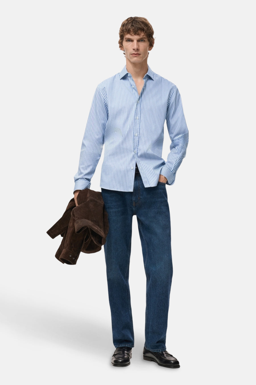 Chemise bleue rayée à manches longues de MANGO, portée avec des jeans et un manteau brun.