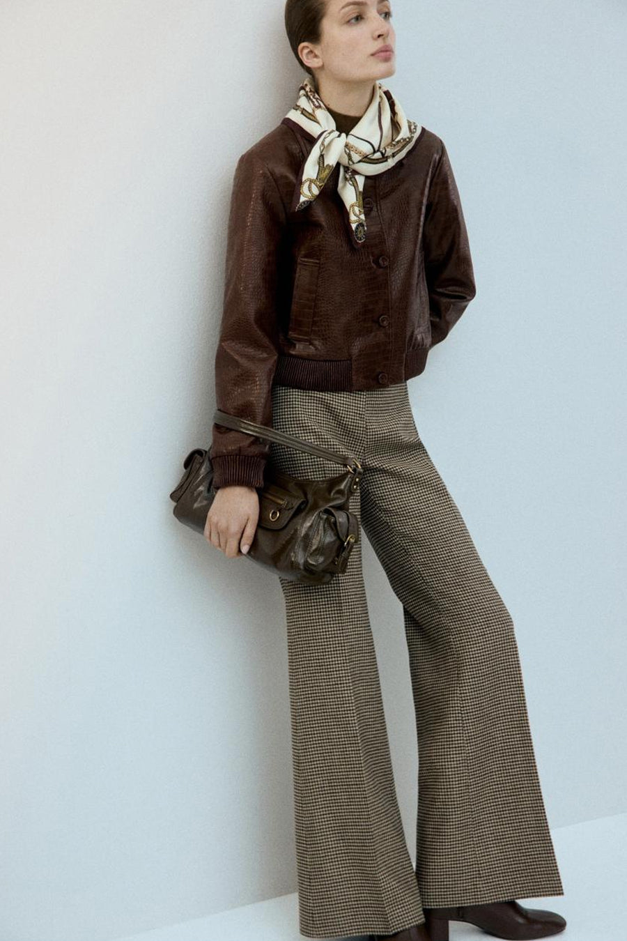 Veste courte marron de MANGO, avec un imprimé crocodile et portée avec une écharpe et un sac à main marron.