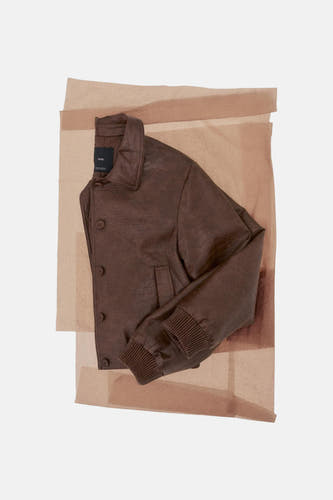 Veste courte marron de MANGO, présentée en couches de papier transparent, avec une texture froissée et des poignets côtelés.