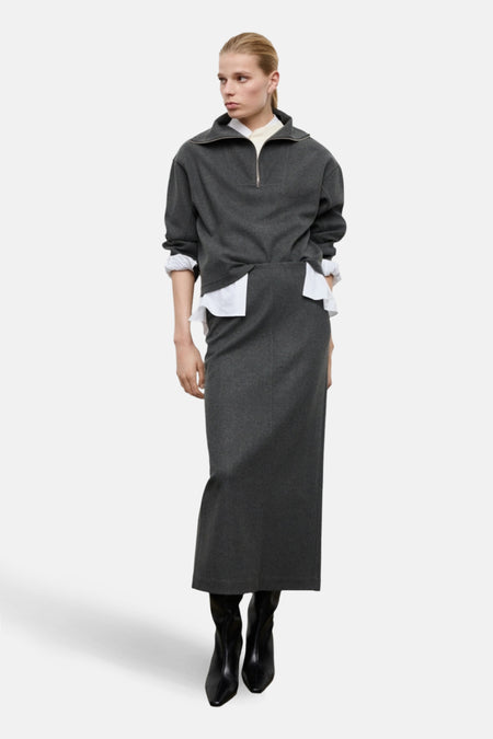 Een vrouw draagt een grijze outfit met een witte blouse en zwarte laarzen.