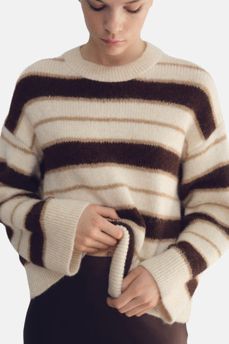 Sweat-shirt multicolore à col rond de MANGO, avec des rayures horizontales et associé à une jupe brune et des bottes noires.