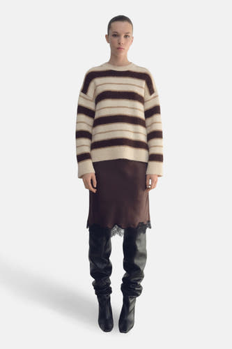 Sweat-shirt multicolore à col rond de MANGO, porté avec une jupe en soie bordée et des bottes noires en cuir.
