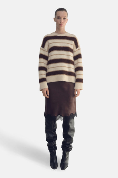 Vrouw in gestreepte trui, bruine rok met kant, en zwarte laarzen.