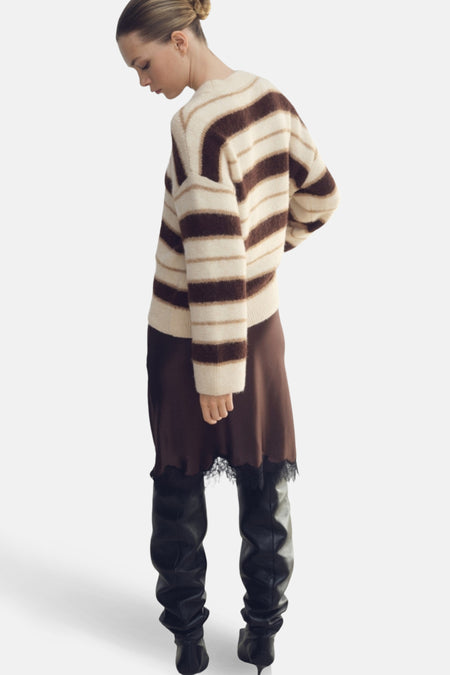 Vrouw in gestreepte trui, bruine jurk en zwarte leren laarzen.