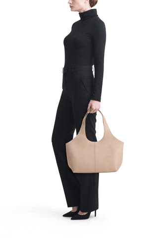 Sac à bandoulière beige de MANGO, porté par un mannequin vêtu d'un col roulé noir et d'un pantalon avec des talons, sur fond blanc.