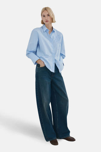 Chemise bleue à manches longues de MANGO, avec motif floral subtil sur le devant, associée à un jean ample et des mocassins marron.