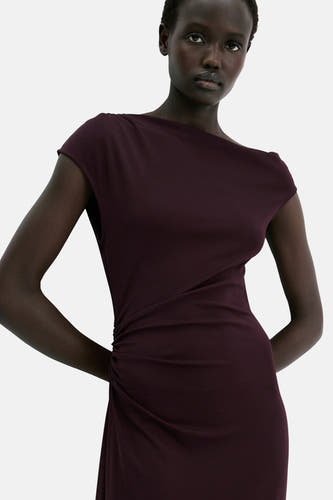 Mouwenloze bordeauxrode kleedje van MANGO, met gedrapeerd detail aan de zijkant en een elegante, asymmetrische halslijn.
