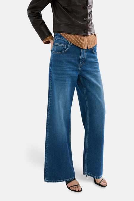 Jean droit bleu NIKI de MANGO, avec jambes larges et poches arrière, combiné avec une veste en cuir marron.