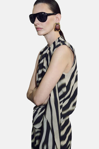 Multikleurige mouwloze blouse van MANGO, met zebraprint en gedrapeerd ontwerp, gecombineerd met vierkante oorbellen en een zonnebril.