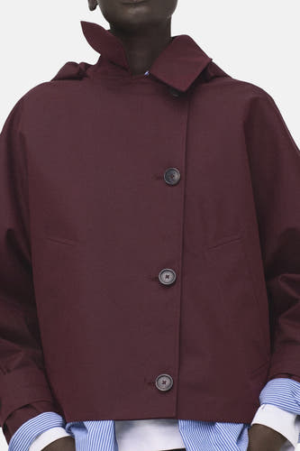 Manteau court bordeaux de MANGO, avec col et manches longues, porté sur une chemise rayée et un jean bleu foncé.