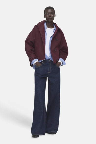 Veste courte bordeaux de MANGO, portée sur une chemise blanche avec une chemise à rayures bleues et un jean ample bleu foncé.