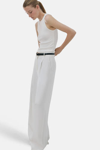 Débardeur blanc de MANGO, avec un col rond et porté avec une ceinture noire et un pantalon blanc.