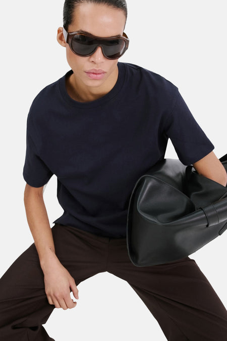 T-shirt bleu de MANGO, vu de dos, avec un pantalon marron et des cheveux tressés.