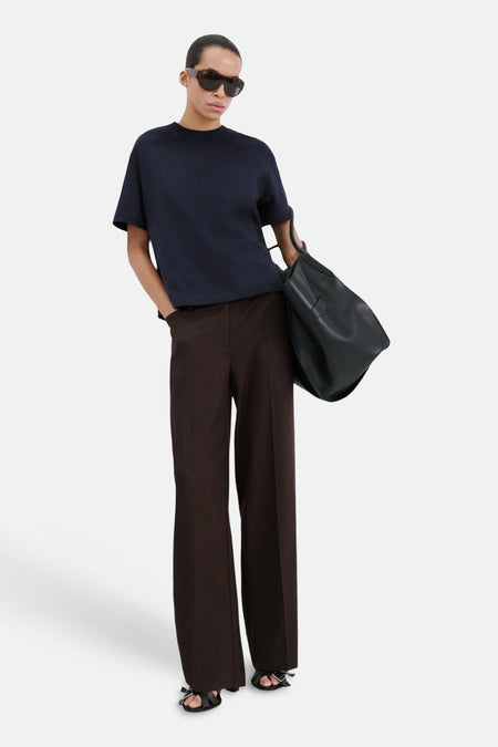 T-shirt bleu à manches courtes de MANGO, associé à un pantalon marron, un sac à main noir et des sandales noires.