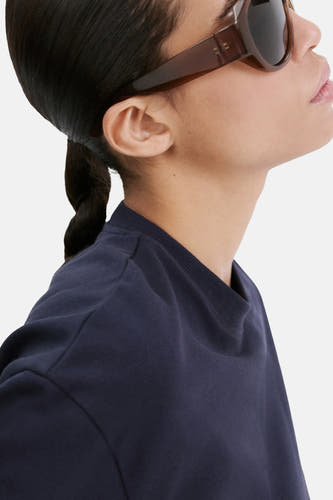 T-shirt bleu de MANGO, à manches courtes et col rond, porté avec des lunettes de soleil marron.