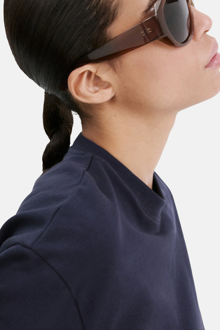 T-shirt bleu de MANGO, à manches courtes et col rond, porté avec des lunettes de soleil marron.