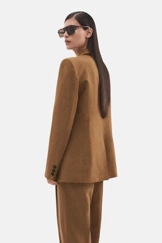 Blazer marron de MANGO avec trois boutons sur la manche, portée par un mannequin avec des lunettes de soleil.