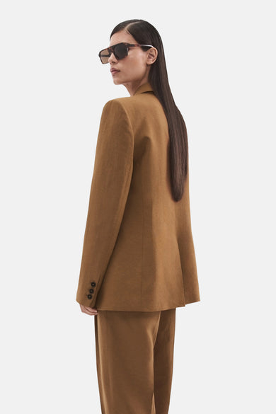 Blazer marron de MANGO avec trois boutons sur la manche, portée par un mannequin avec des lunettes de soleil.