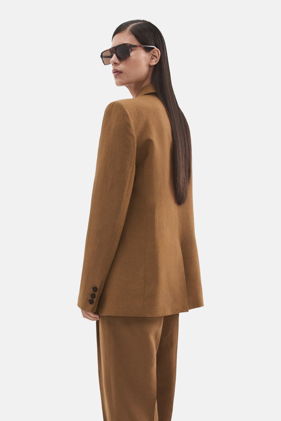 Blazer marron de MANGO avec trois boutons sur la manche, portée par un mannequin avec des lunettes de soleil.