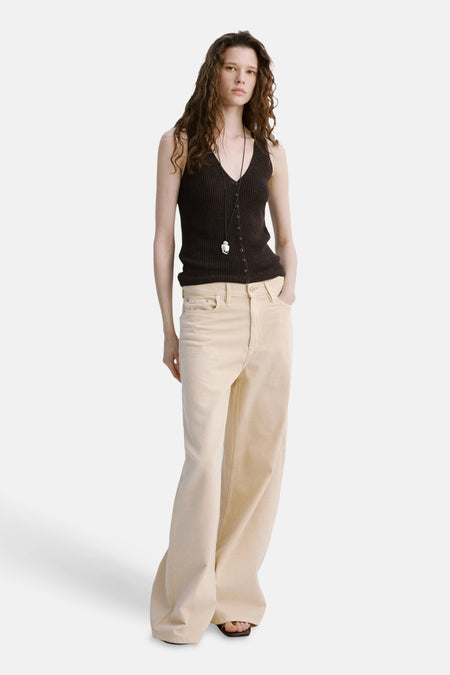Haut marron sans manches de MANGO avec fermeture à boutons, portée avec une chaîne et un pantalon beige.