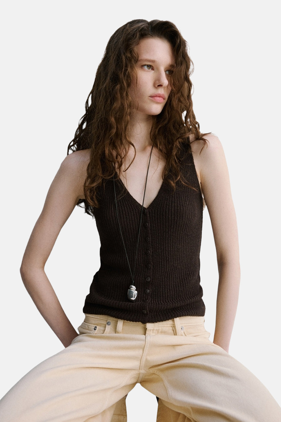 Haut marron sans manches de MANGO, vue de dos avec des cheveux bruns bouclés et un pantalon beige.