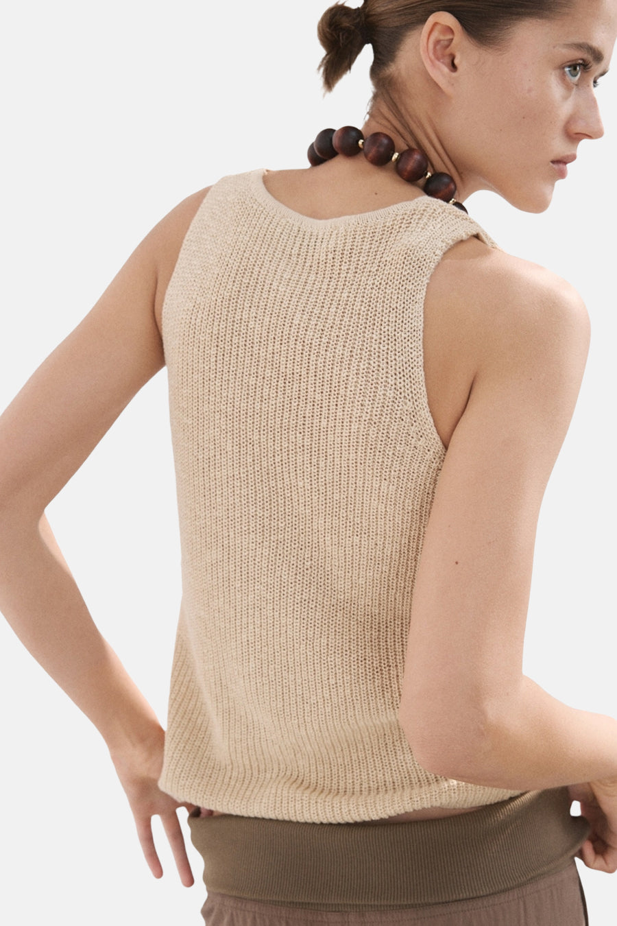 Beige mouwloze top van MANGO, met een gebreide textuur en een ronde halslijn, gecombineerd met een houten ketting.
