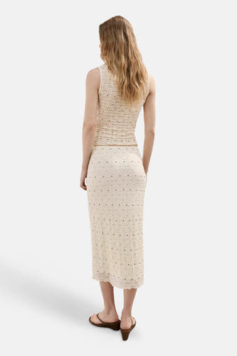 Lange ecru rok van MANGO met gehaakt patroon en kleine bronzen studs, gedragen door model in achteraanzicht.