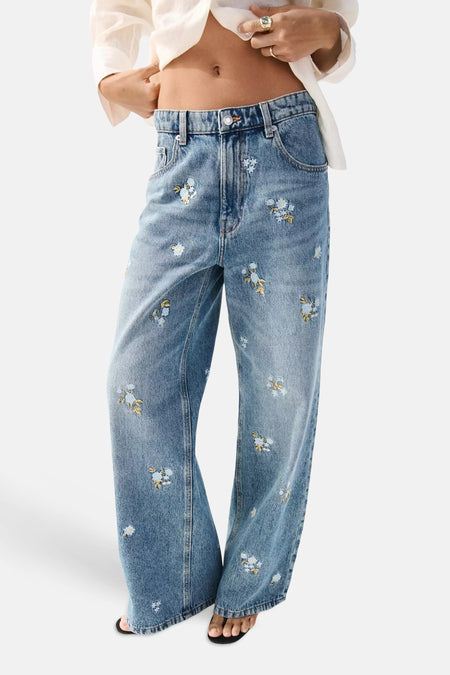 Jean droit en denim bleu clair de MANGO, avec broderies florales, porté à l'arrière par une femme en chemise blanche.
