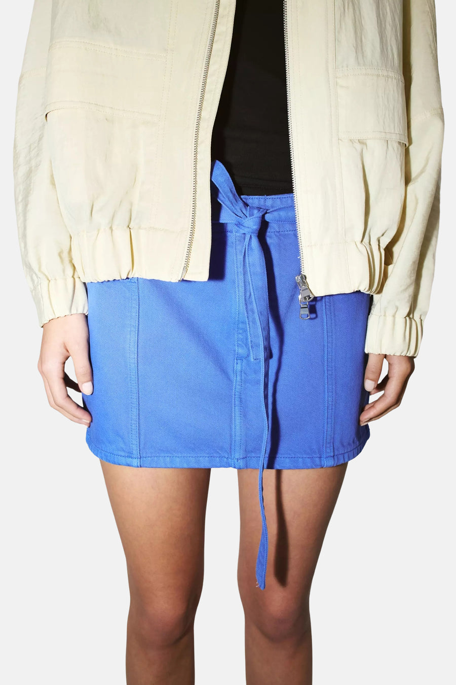 Blauwe denim rok van MANGO met strikdetail, gedragen met crèmekleurige jas en zwart topje, front view