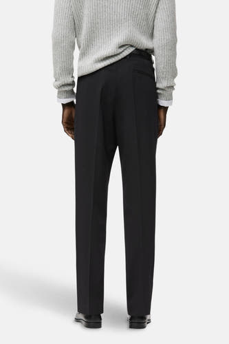 Zwarte broek van MANGO, achterkant, met een effen textuur en gecombineerd met een grijze trui.
