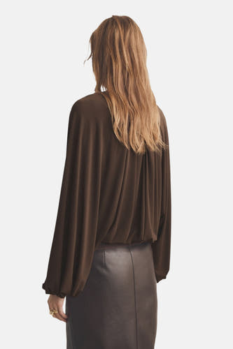 Bruine blouse met lange mouwen van MANGO, gezien van achteren, gecombineerd met een leren rok.
